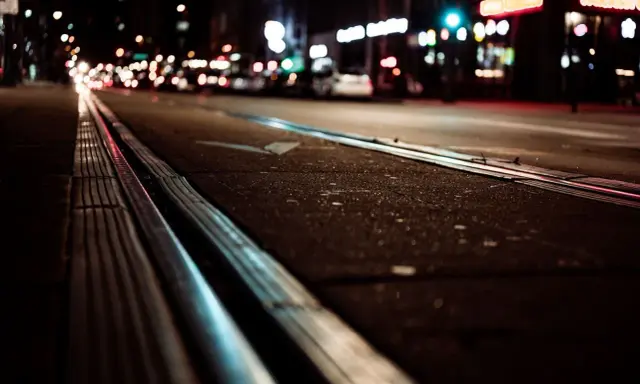 Torowisko tramwajowe w nocy, światła miasta rozmyte, jakby w ślepocie zmierzchowej.