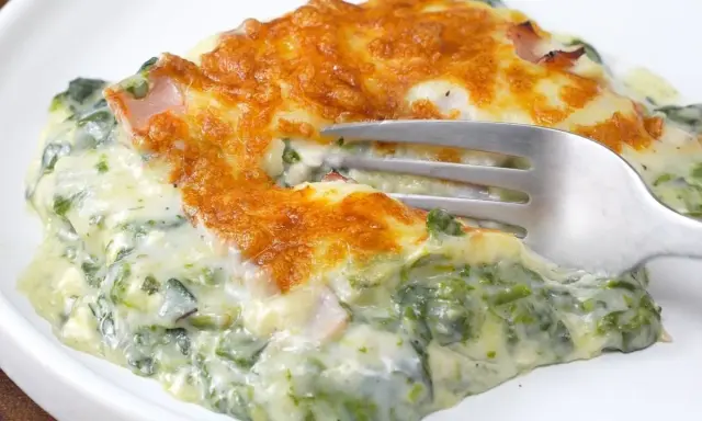 Deliciosa lasaña de espinacas cremosa, gratinada y lista para disfrutar. Un tenedor se hunde en esta maravilla.