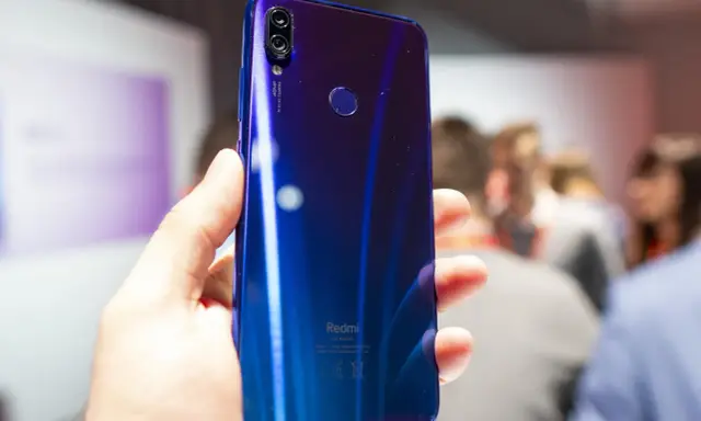 Błyszczący, niebieski tył telefonu Redmi 7 Pro z podwójnym aparatem 48MP i czytnikiem linii papilarnych, trzymany w dłoni.
