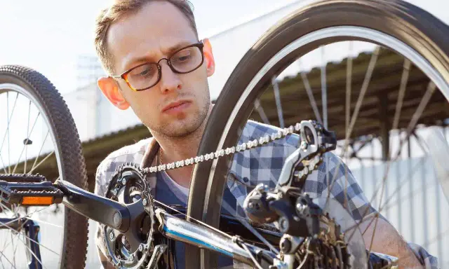 Mężczyzna w okularach sprawdza rozmiary kół rowerowych, skupiony na mechanizmie przerzutek i łańcuchu.