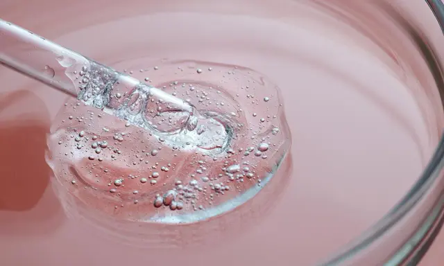 Goccia di siero trasparente con bollicine, su sfondo rosa. Un tocco di vitamina B3 per il viso.