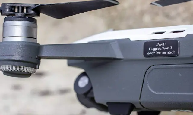 Nahaufnahme einer e-id drohne mit Propeller und Aufkleber "UAV-ID Flugplatz West 3 56789 Drohnenstadt".