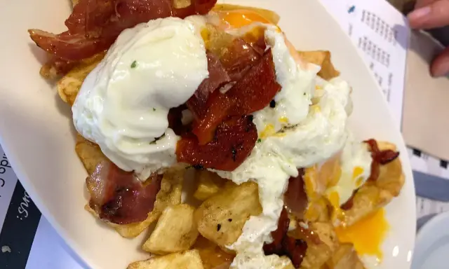 Un plato de patatas fritas con huevos escalfados y jamón, típico de los furanchos de Pontevedra.
