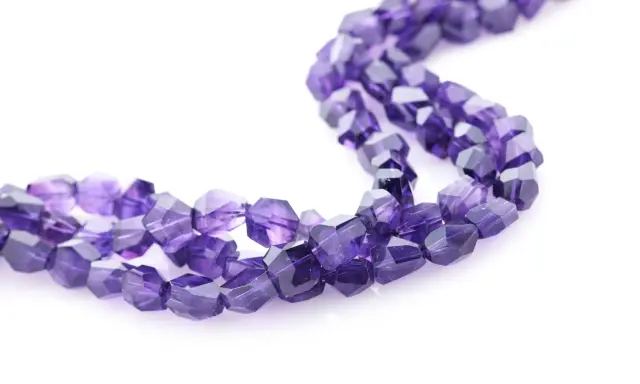 Tre fili di sfaccettate pietre viola, il cui nome è ametista, su sfondo bianco.