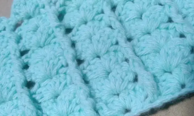 Textura de un tejido a crochet en tono azul claro. Se aprecian los detalles de un punto fantasía, creando un patrón con relieve y pequeños huecos.