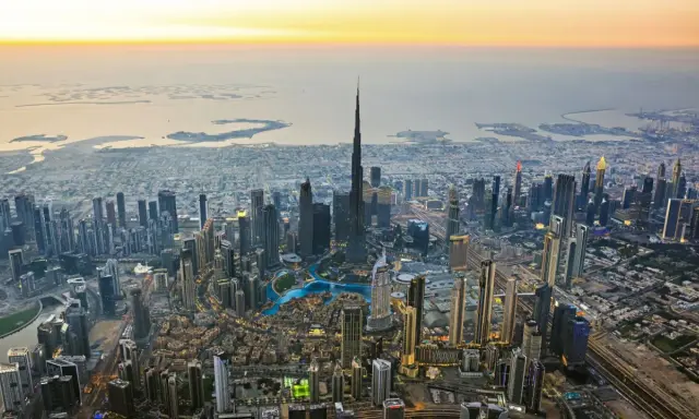 Luftaufnahme von Dubai bei Sonnenuntergang. Der Burj Khalifa ragt empor, umgeben von Wolkenkratzern und den künstlichen Inseln. Ein Blick auf die Dubai Besonderheiten.