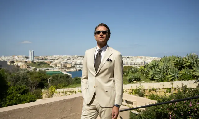 A man in a light tan suit, tie, and sunglasses offers inspiration for what to wear to a communion as a guest male.