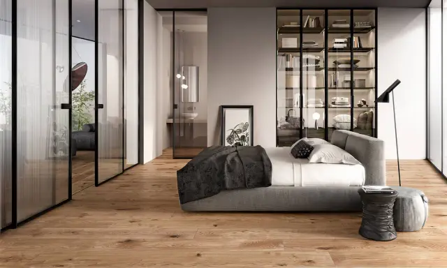 Modern bedroom with glass doors, a bed, and a wardrobe. The doors are designed to transform a hinged door into a sliding one, saving space.