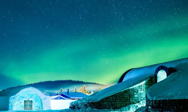 Snöklädda byggnader under norrsken. En magisk plats att se norrsken i Sverige.