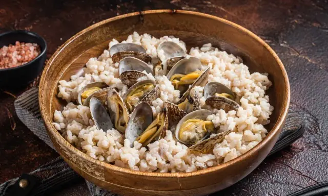 Un delicioso arroz con almejas, servido en un cuenco de madera. Las almejas, abiertas y jugosas, se mezclan con el arroz cremoso.