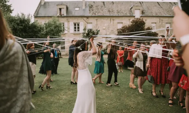 Novia con ramo de flores, rodeada de mujeres con cintas blancas, en el momento cuando se tira el ramo de novia.
