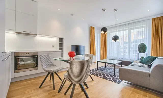 Nowoczesny salon z aneksem kuchennym. Opis pokoju po angielsku: kuchnia z piekarnikiem, szklany stół z krzesłami, sofa, stolik kawowy, dywan.