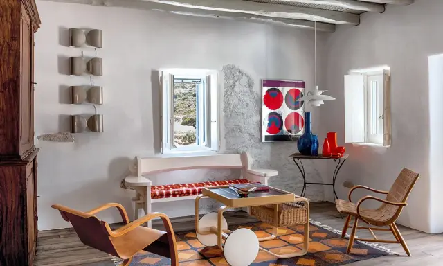Salon d'une typique maison grecque avec mobilier en bois, tapis coloré et vue sur la mer par la fenêtre.