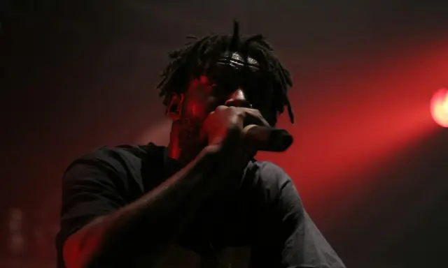 En 90 tals rappare med dreadlocks framför en röd ljusshow, svettig och fokuserad på mikrofonen.
