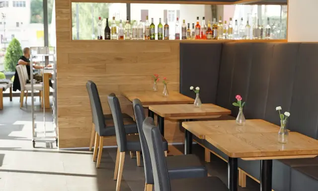 Mesas de madera con floreros y sillas negras en un restaurante. La distancia entre mesas permite un espacio cómodo.