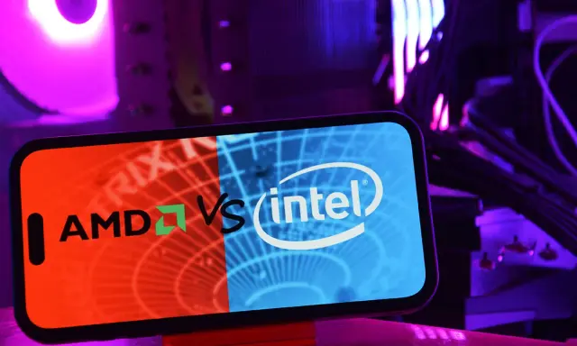 Telefon z logo AMD vs Intel na tle podświetlanego komputera.