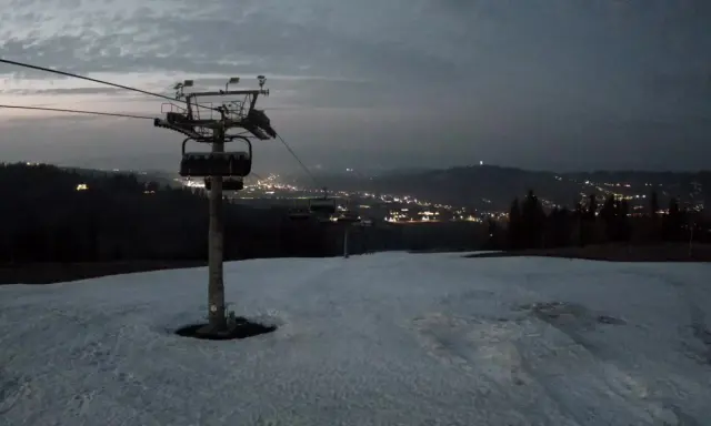 Widok z bukowina ski kamery na ośnieżony stok i nocne światła miasta w oddali.