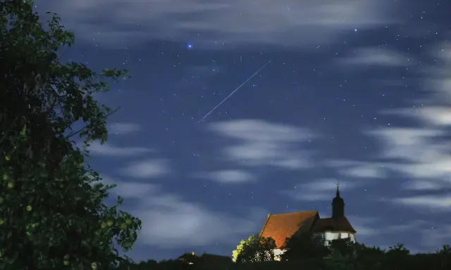 Ein Sternschnuppenregen über einer kleinen Kirche. Man sieht, wann sieht man sternschnuppen, wenn der Himmel klar ist und die Nacht dunkel.