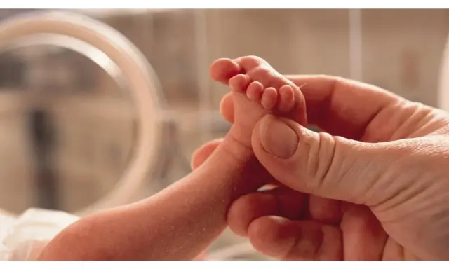Un piedino di neonato tenuto da una mano adulta. Un'immagine che evoca la delicatezza e l'importanza della valutazione Apgar, un test per valutare le condizioni del neonato alla nascita.