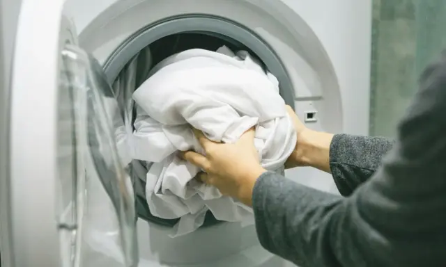 Ręce wkładają białą pościel do pralki. Zastanawiam się, jakie wirowanie w pralce będzie najlepsze dla tej delikatnej tkaniny.