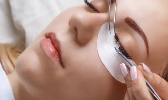 Une esthéticienne utilise des pinces pour appliquer des extensions de cils, une étape clé pour savoir comment coiffer ses sourcils et sublimer le regard.