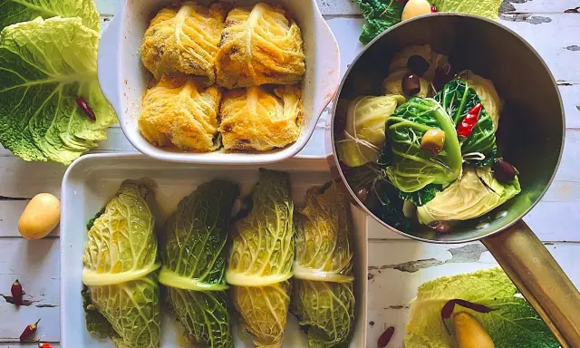Involtini di verza pronti per essere cotti, alcuni impanati, altri legati con filo, con patate e peperoncini intorno.