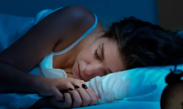 Kobieta śpi, ale budzik sugeruje, że to może być kolejna noc bez snu. Co to insomnia?