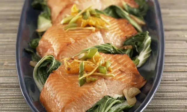Saftiger Lachs mit Mangold, garniert mit Ingwer und Frühlingszwiebeln, auf einem dunkelblauen Teller serviert.