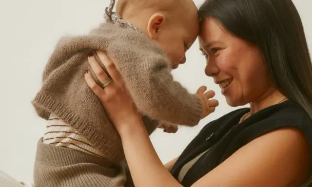 Madre y bebé se miran con ternura, frente con frente. El bebé, envuelto en un suéter de lana, muestra el apego infantil.