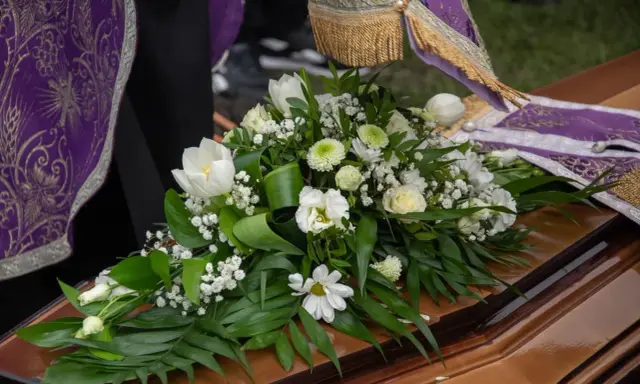 Białe lilie i inne kwiaty na trumnie, symbol pożegnania. Uroczysty bukiet na pogrzeb.