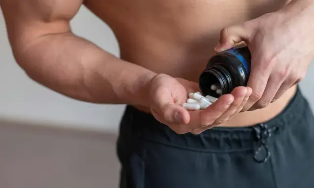 Muskulöser Mann nimmt Kapseln ein, um die BCAA Wirkung für den Muskelaufbau zu nutzen.