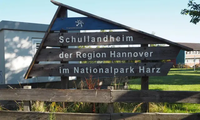 Drewniany drogowskaz "Schullandheim der Region Hannover im Nationalpark Harz" zapowiada przygodę w górach w Niemczech, być może z widokiem na szczyt Brocken.