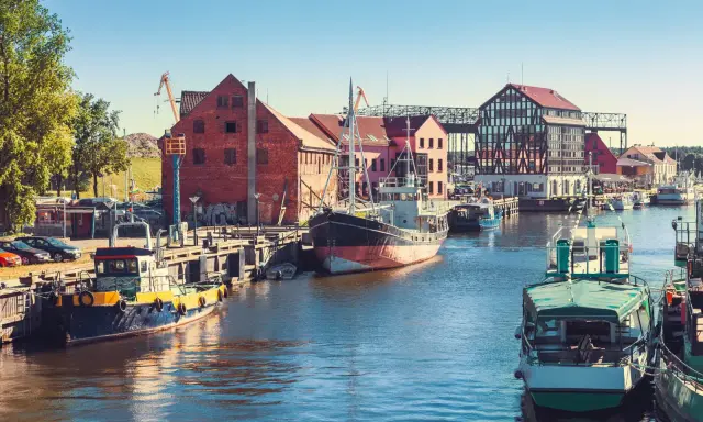 Barche ormeggiate nel porto di Klaipeda, Lituania, con edifici storici e gru sullo sfondo.