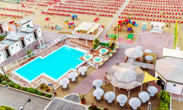 Vista aerea del lido delle sirene Cattolica: piscina, vasche idromassaggio, lettini rossi e ombrelloni sulla spiaggia.