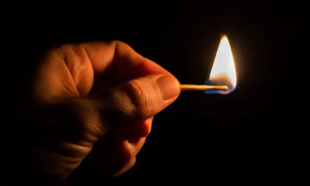 Dłoń trzyma płonącą zapałkę. Czy Polsce grozi blackout? Mały płomień symbolizuje niepewność.