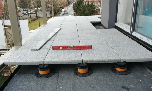 Budowa tarasu wentylowanego. Płyty betonowe ułożone na regulowanych wspornikach, poziomica wskazuje idealne wypoziomowanie.