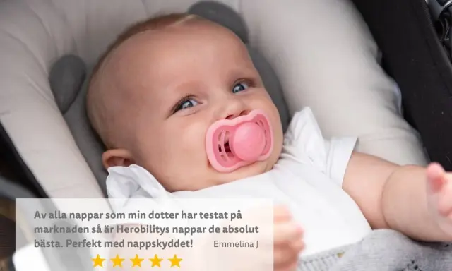 Söt bebis med rosa napp i munnen, som verkar nöjd. En recension lyfter fram nappens kvalitet.