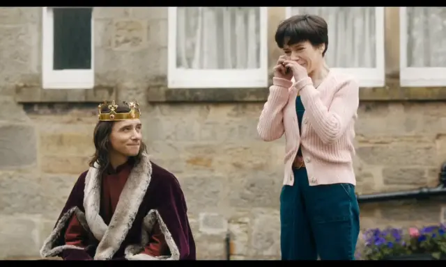 Un re con la corona e la pelliccia, forse il protagonista di "the lost king film", guarda una donna che ride con le mani sul viso.