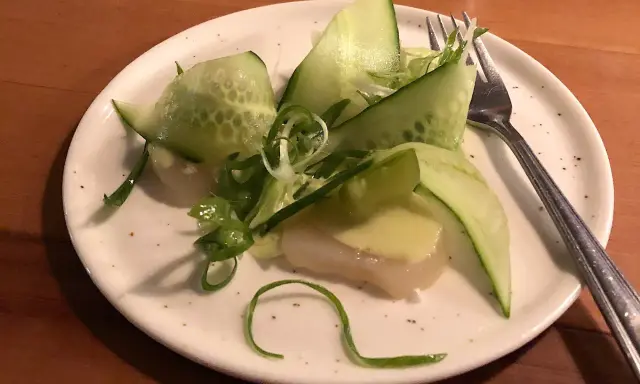 En läcker pilgrimsmussla med gurka och salladslök, serverad på en tallrik i en mysig wood restaurang.