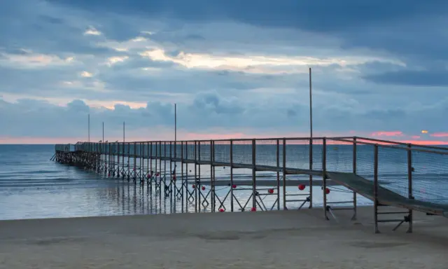 Molo di Rimini Rivazzurra al tramonto, con cielo nuvoloso e mare calmo.