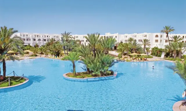 Słoneczny basen w Djerba Resort (dawniej Vincci) otoczony palmami i białymi budynkami.