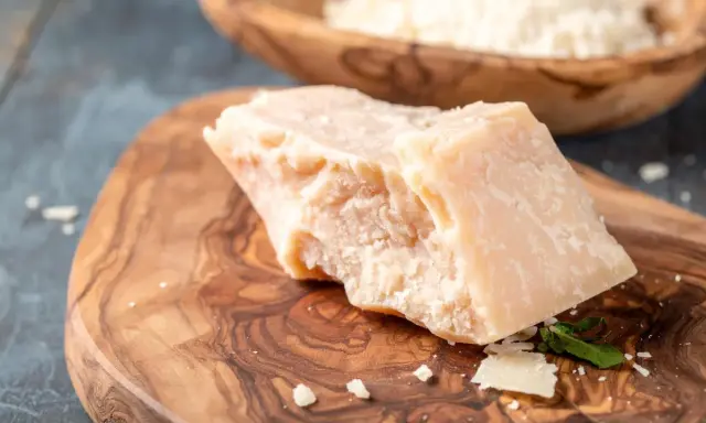 Kawałek twardego sera, przypominającego Grana Padano i parmezan, leży na drewnianej desce.