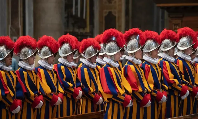 Guardia svizzera pontificia in divisa storica, con elmi piumati e abiti a righe blu, gialle e rosse, in posa solenne.