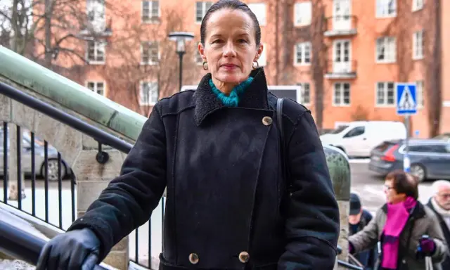 Malin Berghagen, trots att hon verkar sjuk, går uppför en trappa i en svart kappa.
