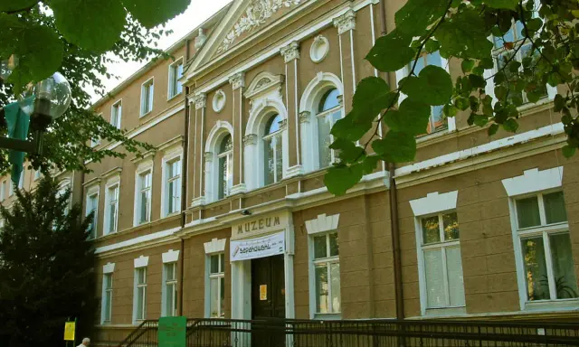 Fasada muzeum w Zielonej Górze, z napisem "MUZEUM". W pobliżu drzewa i ławka.