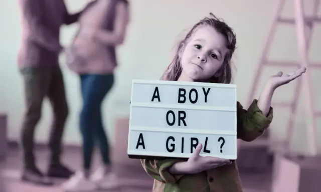 Dziewczynka trzyma tabliczkę "A BOY OR A GIRL?". Rodzice czekają na dziecko, a płeć można poznać do 20. tygodnia ciąży.