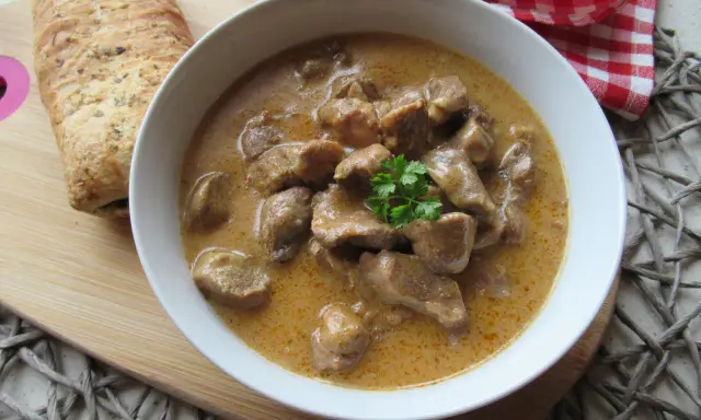 Aromaticzny gulasz wieprzowy w kremowym sosie, udekorowany natką pietruszki, podany z chrupiącym pieczywem.