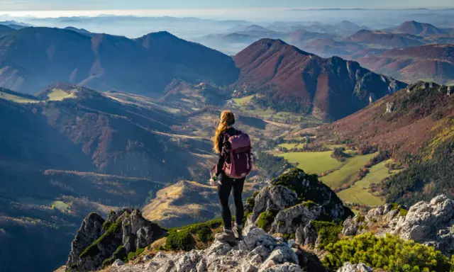Widok na jesienne pasmo górskie Mała Fatra. Kobieta z plecakiem podziwia panoramę z kamienistego szczytu.