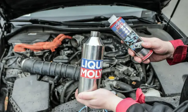 Ręce trzymające preparaty Liqui Moly do czyszczenia katalizatora. W tle widać silnik samochodu.