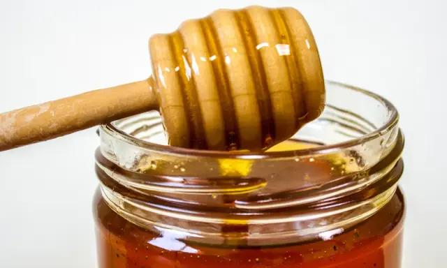 Słoik z miodem i drewniana łyżka do miodu. Naturalny antybiotyk na gardło, który pomoże złagodzić ból.